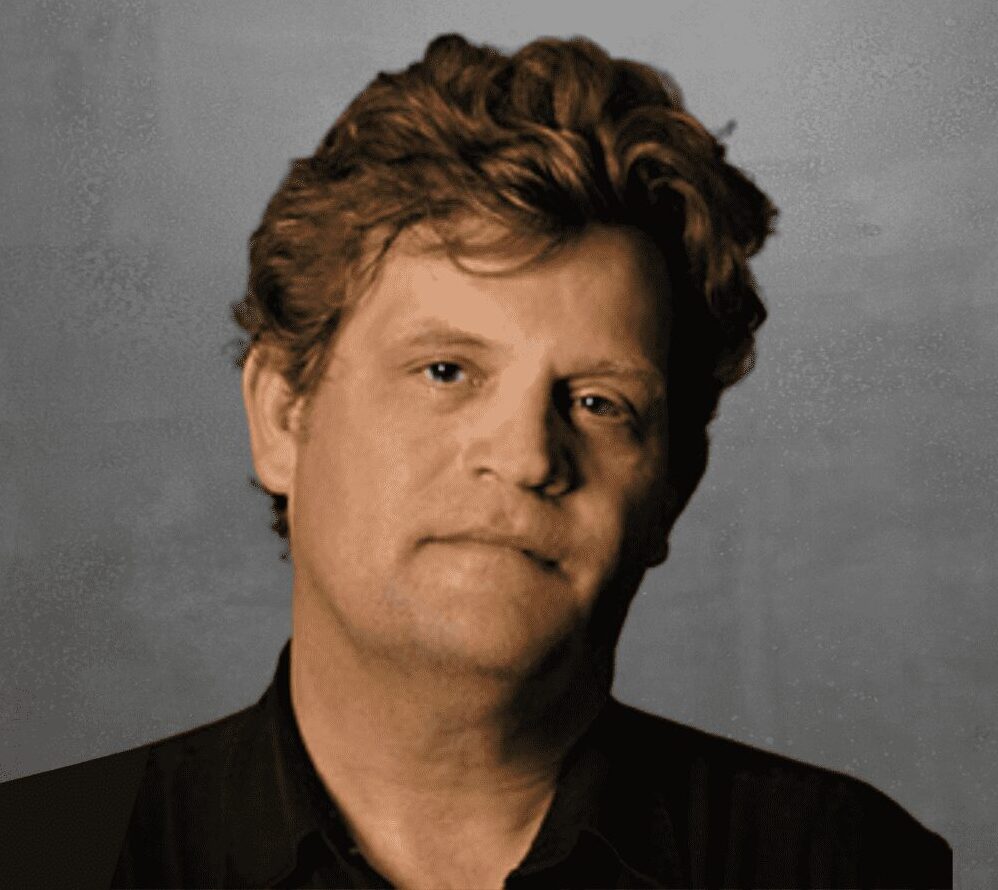 Portrait of a man with curly hair against a gray background.
