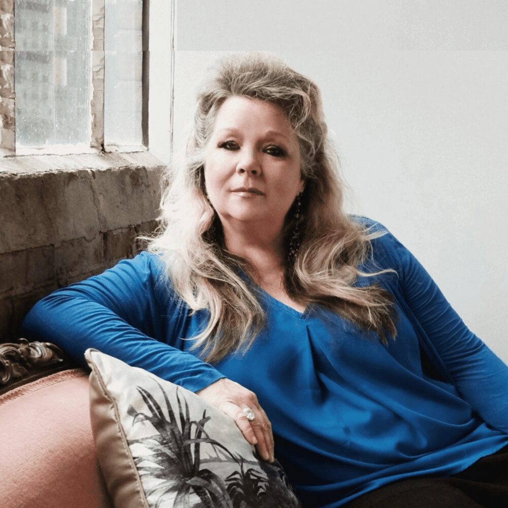 A relaxed woman sitting on a sofa by a window.