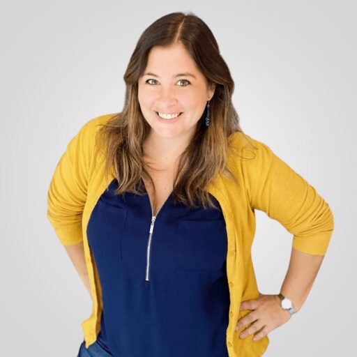 Smiling woman in a yellow cardigan and navy blouse posing against a gray background.