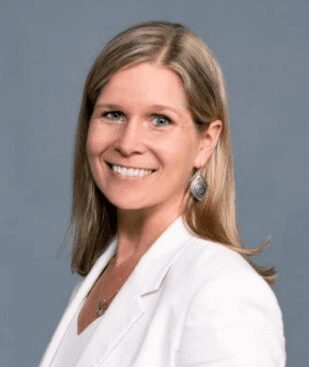 A professional woman smiling in a white blazer against a gray background.