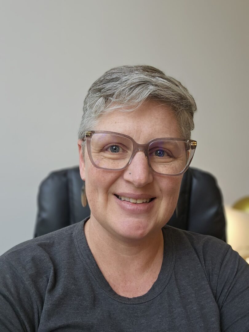 Smiling person with glasses and short gray hair